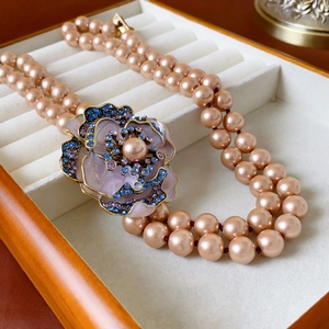 Detailed macro view of vintage camellia pendant and double-layered champagne pearl necklace