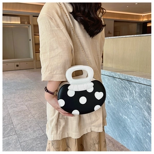 Polka dot heart handbag with gold chain strap and white curved handle shown on a model