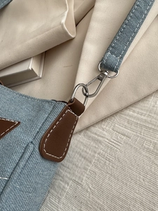 Macro detail of denim shoulder bag with leather reinforcement and silver metal buckle