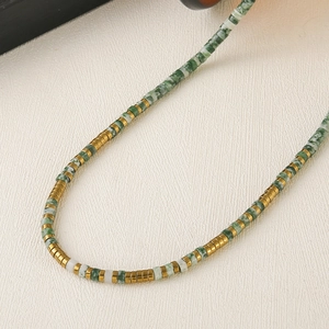 Ethnic style necklace with green marble beads and golden metal cylinders on white leather