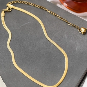 Elegant gold snake bone chain necklace with a delicate heart pendant on a stone background