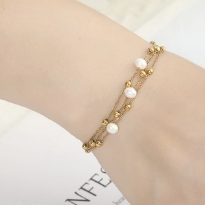 Detail of double-layer gold chain bracelet with white pearls and beads on wrist