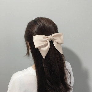 Detail of cream satin bow hair clip on dark brown wavy hair in elegant style