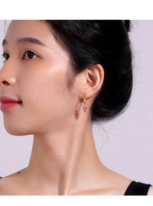 Close-up of gold earrings with pink heart-shaped crystal zircon worn by a model
