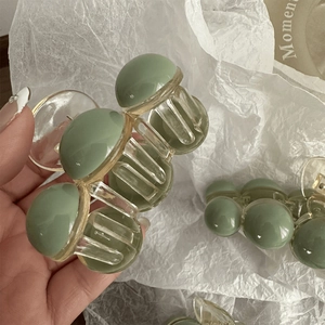Detail of a matte green plastic hair claw clip with transparent teeth held by hand