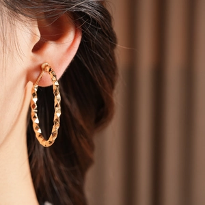 Close-up of golden geometric C-shape hoop earrings with diamond-cut texture on model