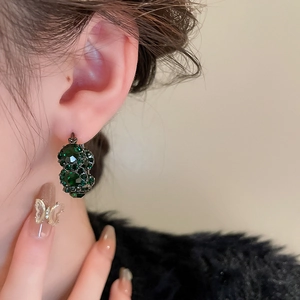 Elegant vintage hoop earrings with green crystal inlay worn by a model in close-up shot