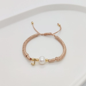 Macro detail of hand-woven beige rope bracelet with pearl and golden J initial charm