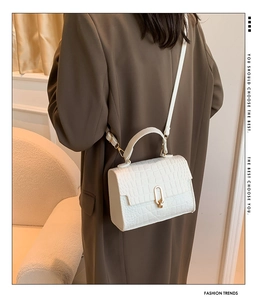 Detail of white crocodile pattern handbag with gold U-shaped buckle on brown blazer