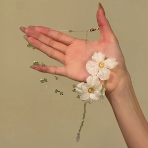 Detailed view of handmade white fabric flowers and green beads on a delicate necklace