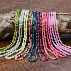Close-up of vibrant pink tourmaline and natural stone beaded necklaces on rustic wood