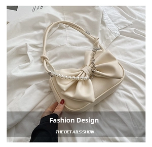 Detail of cream shoulder bag featuring a large bow, pearl beads, and silver chain accent