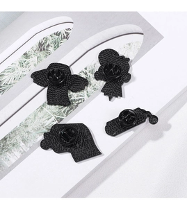 Detail view of four black metal enamel pins showing textured backs and butterfly clasps