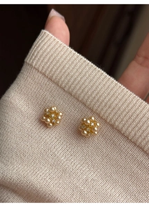 Macro view of floral pearl earrings with gold metal base on a beige knit fabric