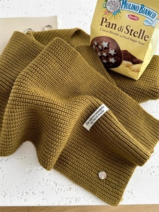 Dettaglio della maglia spessa giallo senape con etichetta bianca e bottone in conchiglia