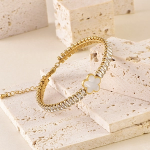 Golden bracelet with square crystals and central white flower on beige textured stone