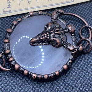 Detail of vintage copper skull pendant with round clear quartz stone on dark texture