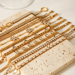 Detailed view of layered gold bracelets with zircon charms on a stone surface