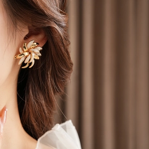 Macro close-up of a vintage gold-plated floral earring with white enamel details on a model
