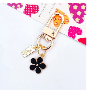 Detail of gold metal keychain with black floral charm and engraved handmade tag