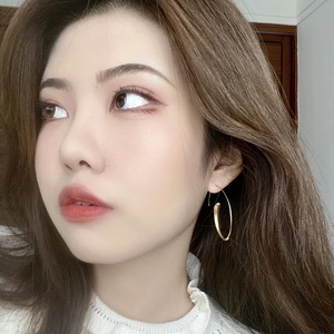 Close-up of a model wearing matte gold C-shaped geometric hoop earrings in a studio setting