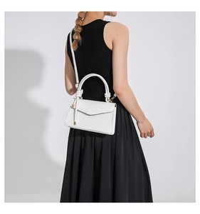 Detailed view of a white woven texture crossbody bag on a model in a black dress