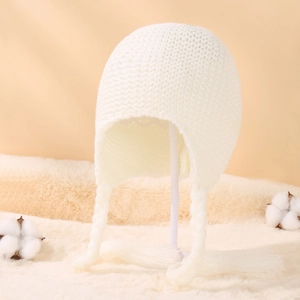 Macro detail of creamy white chunky knit baby hat with ear flaps and braided tassels