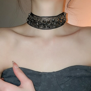 Détail d'un ras de cou floral en dentelle noire orné de strass gris foncé sur le cou