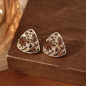 Detail view of triangle earrings with brown amber crystals on a textured brown surface