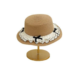 Sweet straw sun hat with white ruffled lace and black velvet bow on a golden stand