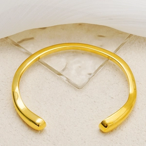 Close-up of irregular 18K gold plated titanium steel open bangle on silk background