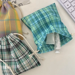 Three plaid drawstring pouches in green, blue, and yellow patterns on a desk