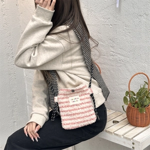 Pink and white striped plush crossbody bag shown worn by a model in a minimal setting