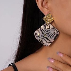Close-up of geometric acrylic earrings with marble texture and hammered gold square