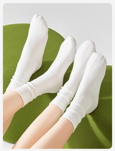 Close-up of lightweight white cotton crew socks worn by a model on a green sofa