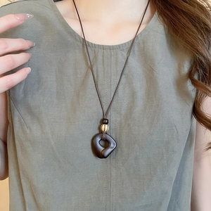 Close-up of vintage resin wood pendant with tassels on a brown woven necklace cord
