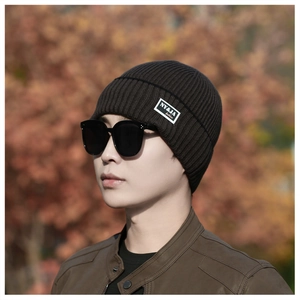 Detail of dark brown ribbed knit beanie featuring a white rectangular fashion label