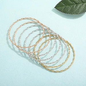 Detail von sieben gedrehten Metallarmreifen in Gold, Silber und Roségold Tönen