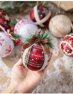 Detail of a red plaid Christmas ball with pine needles and cones held by a hand