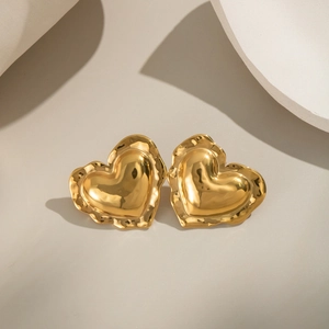 Close-up of 18K gold plated heart earrings with irregular hammered texture on gray surface