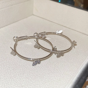 Macro shot of silver hoop earrings featuring intricate small butterfly charms on jewelry box