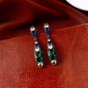 Macro detail of vintage teardrop earrings with colorful zircons on brown leather surface