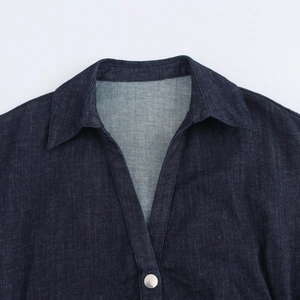 Dettaglio del collo a V e bottone in metallo argento su tessuto denim blu scuro