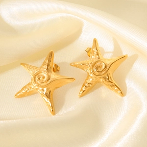 Macro detail of gold-plated starfish earrings with textured surface on beige silk