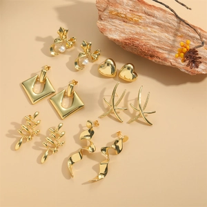 Collection of elegant gold heart, bow and geometric earrings on a warm textured background