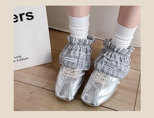 Detail of checkered ruffle leg warmers with silver metallic sneakers on wooden floor