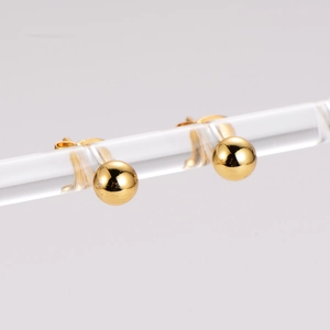 Vue détaillée de boucles d'oreilles boules dorées polies sur support acrylique