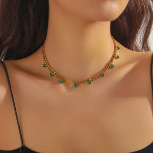Detailed view of a gold chain necklace with green teardrop gemstones on a model's neck
