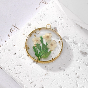 Macro detail of round gold pendant with real white daisy flowers and gold foil flakes