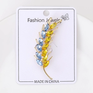 Macro detail of golden wheat ear brooch featuring sparkling blue and yellow crystals